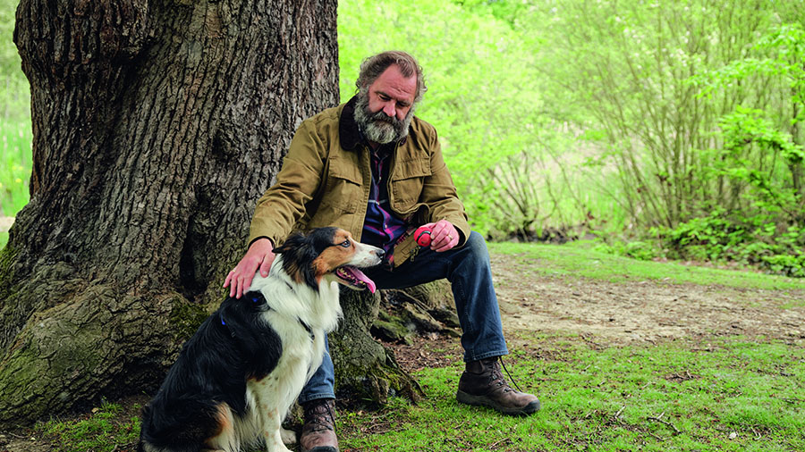 Older man sitting against tree with dog